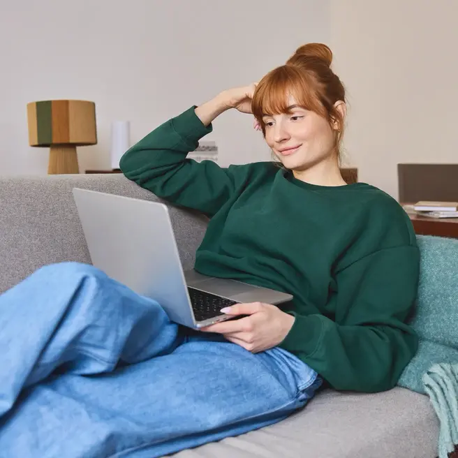 Eine Person liegt entspannt auf einem Sofa und arbeitet an einem Laptop in einem modern eingerichteten Raum &ndash; ein Moment digitaler Flexibilit&auml;t, wie sie der Mobilfunkanbieter yelllow.at unterst&uuml;tzt.