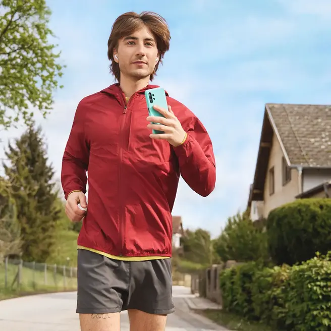 Eine Person joggt durch eine Wohnstra&szlig;e und h&auml;lt dabei ein Smartphone &ndash; ein Moment moderner Mobilit&auml;t, wie sie der Mobilfunkanbieter yelllow.at bietet.