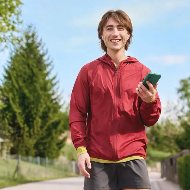 Eine Person joggt durch eine Wohnstra&szlig;e und h&auml;lt dabei ein Smartphone &ndash; ein Moment moderner Mobilit&auml;t, wie sie der Mobilfunkanbieter yelllow.at bietet.