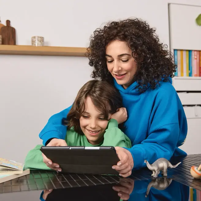 Mutter und ein Kind sitzen in einer K&uuml;che und schauen gemeinsam auf ein Tablet &ndash; ein Moment digitaler N&auml;he mit yelllow.at.