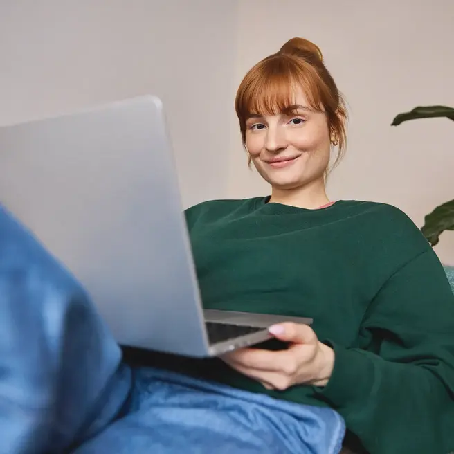 Eine Person liegt entspannt auf einem Sofa und arbeitet an einem Laptop in einem modern eingerichteten Raum &ndash; ein Moment digitaler Flexibilit&auml;t, wie sie der Mobilfunkanbieter yelllow.at unterst&uuml;tzt.