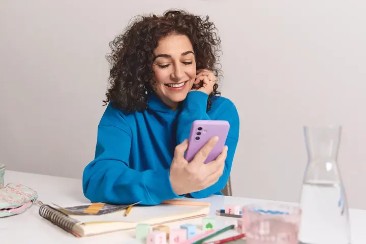 Eine Person sitzt an einem Tisch mit Unterlagen und blickt auf ein Handy &ndash; ein Moment digitaler Organisation, unterst&uuml;tzt von yelllow.at.