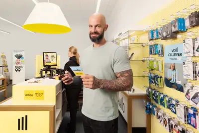 T&auml;towierter Mann steht mit SIM in der Hand in der Postfiliale