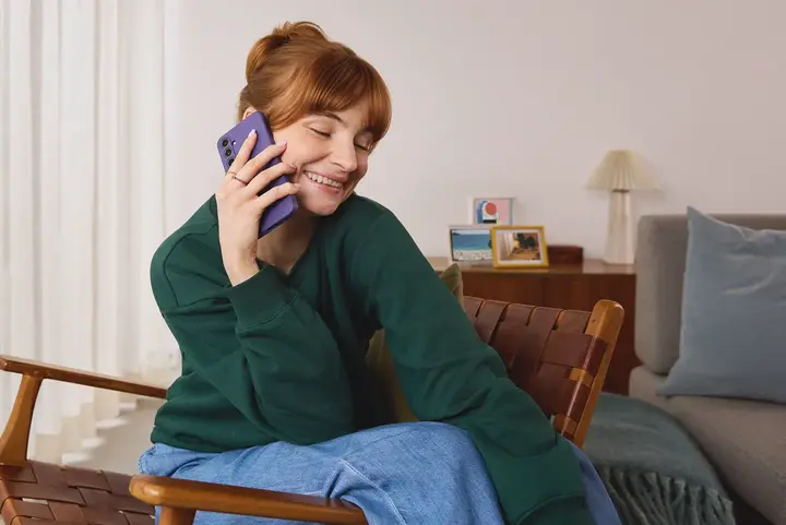 Eine Person sitzt in einem hellen Wohnzimmer auf einem Stuhl und telefoniert mit einem Handy &ndash; ein allt&auml;glicher Moment moderner Kommunikation, wie sie yelllow.at erm&ouml;glicht.