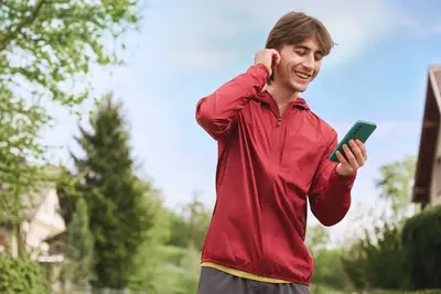 Eine Person joggt durch eine Wohnstra&szlig;e und h&auml;lt dabei ein Handy &ndash; ein Moment moderner Mobilit&auml;t, wie sie der Mobilfunkanbieter yelllow.at bietet.