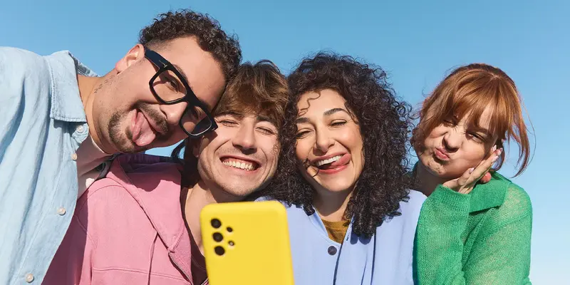 Vier Personen machen im Freien ein Selfie mit einem gelben Handy.