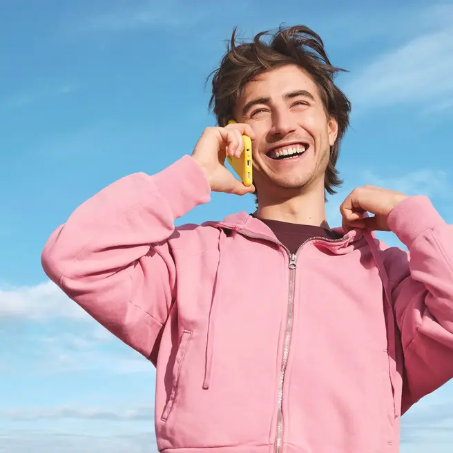 Eine Person steht vor blauem Himmel und telefoniert mit einem gelben Smartphone &ndash; passend zum Stil des neuen Mobilfunkanbieters yelllow.at.
