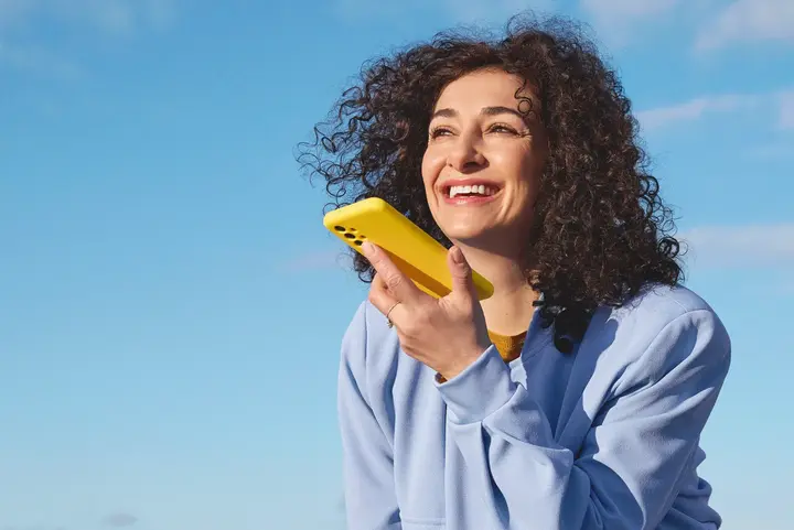 Eine Person steht auf einer Dachterrasse &uuml;ber der Stadt und h&auml;lt ein gelbes Smartphone in der Hand &ndash; passend zum Stil des neuen Mobilfunkanbieters yelllow.at.