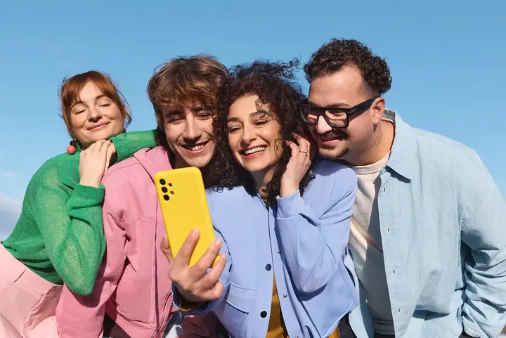Vier Personen machen im Freien ein Selfie mit einem gelben Handy.