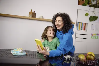 Eine junge Mutter schaut zusammen mit ihrem Kind am K&uuml;chentisch in ihr Smartphone mit YELLLOW Tarif.